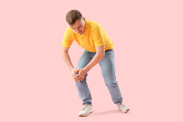 Young man suffering from knee pain on pink background