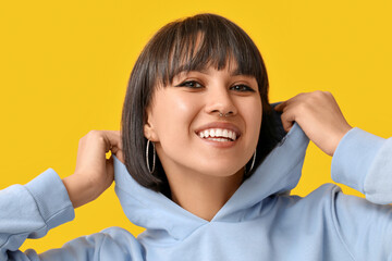 Happy stylish young woman with nose piercing on yellow background