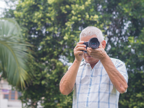 Senior man taking photo with camera in the garden.