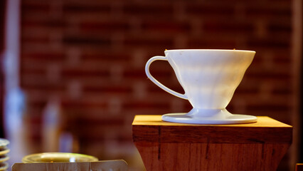 Empty ceramic white cup stands on wooden table of coffee shop against blurred brick wall.