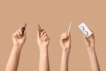 Female hands with lipsticks, fake lashes and eyeliner on beige background