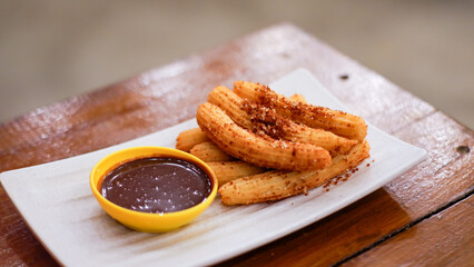Churros with brown sugar and chocolate sauce on wooden table