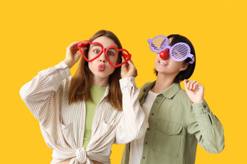Beautiful young women in funny disguise on yellow background. April Fools Day celebration