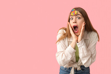 Beautiful young shocked woman with paper fish attached to her forehead on pink background. April...