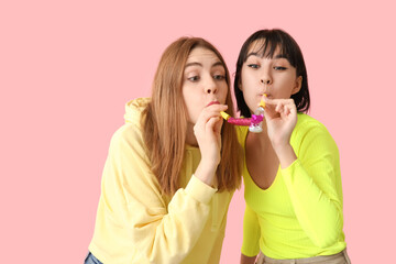 Beautiful young women with party whistles on pink background. April Fools Day celebration