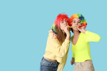 Beautiful young women in funny clown disguise with party whistles on blue background. April Fools...
