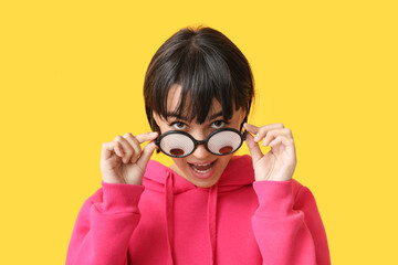Beautiful young woman in funny disguise on yellow background. April Fools Day celebration