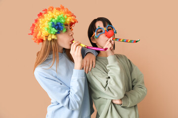 Beautiful young women in funny clown disguise with party whistles on brown background. April Fools...