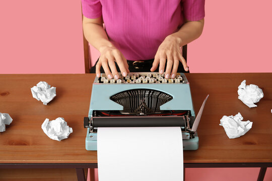 Young woman with vintage typewriter at table on pink background - Powered by Adobe