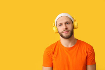 Young man in modern headphones on yellow background