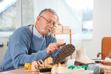 Male shoemaker brushing boot at table in workshop - obrazy, fototapety, plakaty