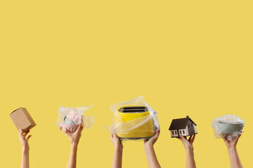 Women with moving box, wrapped dishes, toaster and house model on yellow background