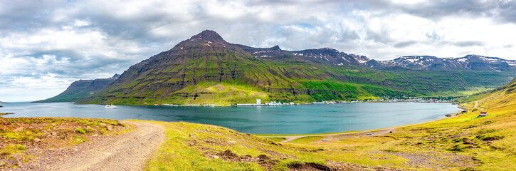 Panoramic with lagoon and fjords in East Iceland, near Seydisfjordur with dramatic sky and green meadow hills. Beautiful Icelandic landscape, huge cliff, ocean, and rock in moss
