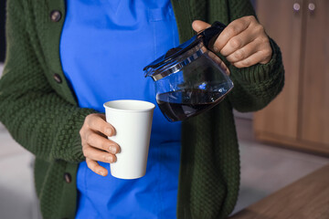 Female nurse pouring coffee at hospital in evening, closeup