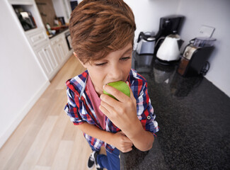 Face, kitchen and boy biting apple in home as diet, health or nutrition for child development...