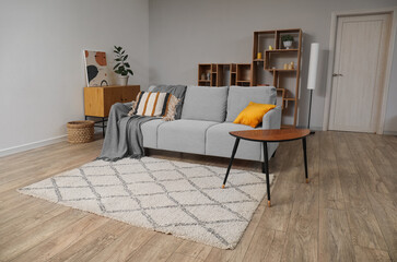 Stylish grey sofa with coffee table and carpet on floor in living room