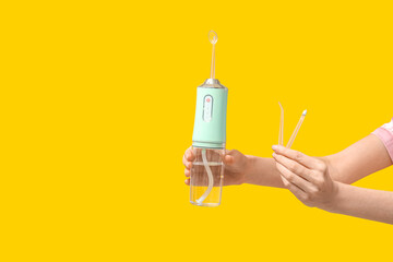 Female hands with oral irrigator on yellow background