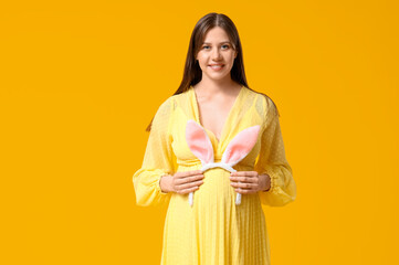 Beautiful young pregnant woman with bunny ears on yellow background. Easter celebration