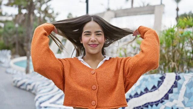 Smiling young woman in an orange cardigan poses playfully outdoors, capturing a sense of cheer and youthfulness.