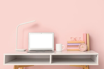 Stylish workplace with desk, laptop and books near pink wall
