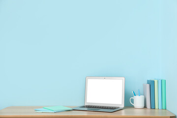 Stylish workplace with books and laptop near blue wall