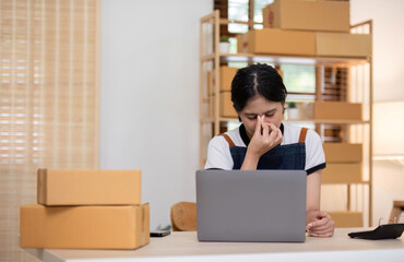 A young Asian entrepreneur feels stressed while selling online through online platforms because she has trouble organizing orders and packing products into boxes for delivery.