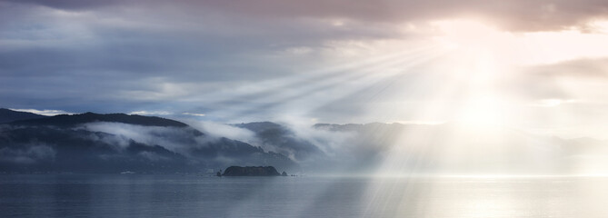 Sun rays, sea and clouds in blue sky with mountains, water and fog in evening. Lake, landscape and...