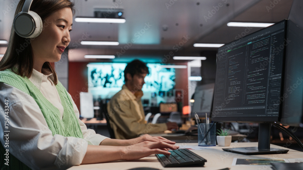 Poster Female Asian Game Programmer Coding On Desktop Computer In Game Development Studio Diverse Office. Focused Woman Writes Lines Of Code, Does Gameplay Engineering For New Immersive 3D RPG Video Game
