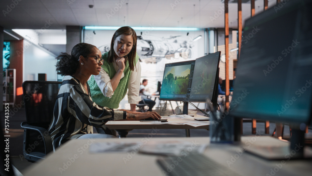 Poster Black Female Game Designer Using Desktop Computer With 3D modelling Software And Talking to Asian Female Project Manager in Game Development Studio Office. Diverse Colleagues Discussing New RPG Game