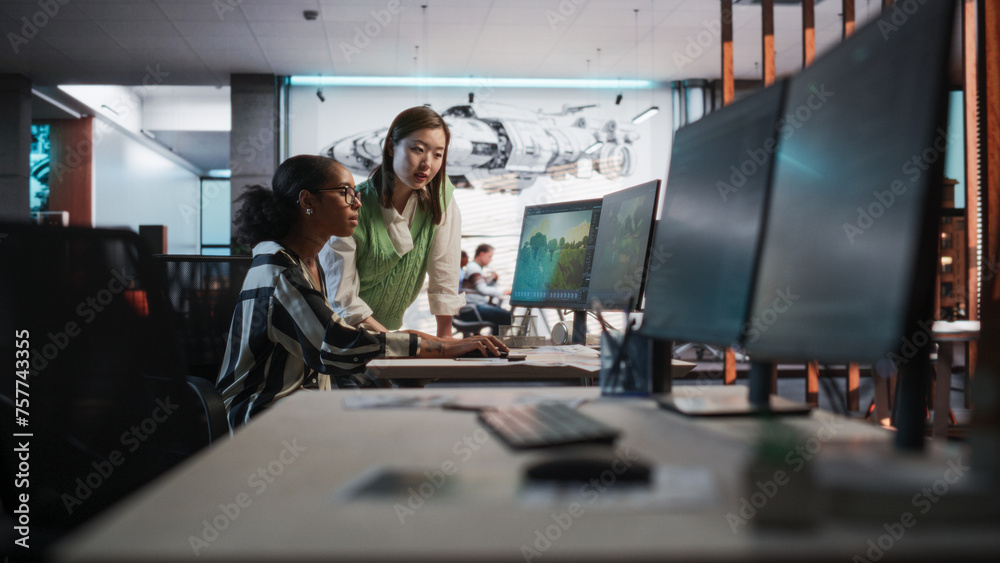 Poster Black Female Game Developer Using Desktop Computer With 3D modelling Software And Talking to Asian Female Project Manager in Game Design Studio Office. Two Diverse Colleagues Discussing New RPG Game