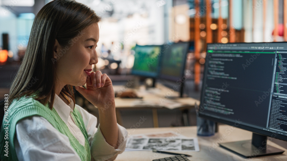 Fototapete Female Asian Game Programmer Coding On Desktop Computer In Game Development Studio Diverse Office. Focused Woman Writes Lines Of Code, Does AI Engineering For New Immersive 3D Survival Video Game