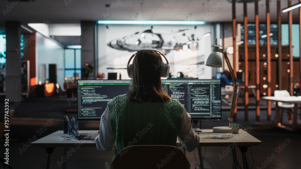 Poster Creative Office: Professional Female Programmer Uses Headphones, Working on Desktop Computer. Focused Coder, Software Engineer Developing App, Video Game. Listening to Podcast or Music. Back View.