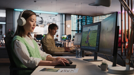 Female Asian Game Designer Using Desktop Computer, Designing Unique World And Characters In 3D modelling Software For RPG Video Game. Woman Working In Diverse Game Development Studio Office