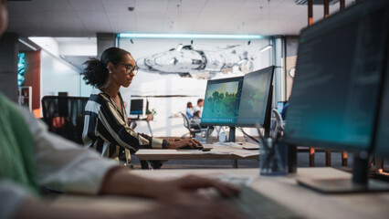 Black Female Game Developer Using Desktop Computer With 3D modelling Software And Talking to Asian Female Project Manager in Game Design Studio Office. Two Diverse Colleagues Discussing New RPG Game