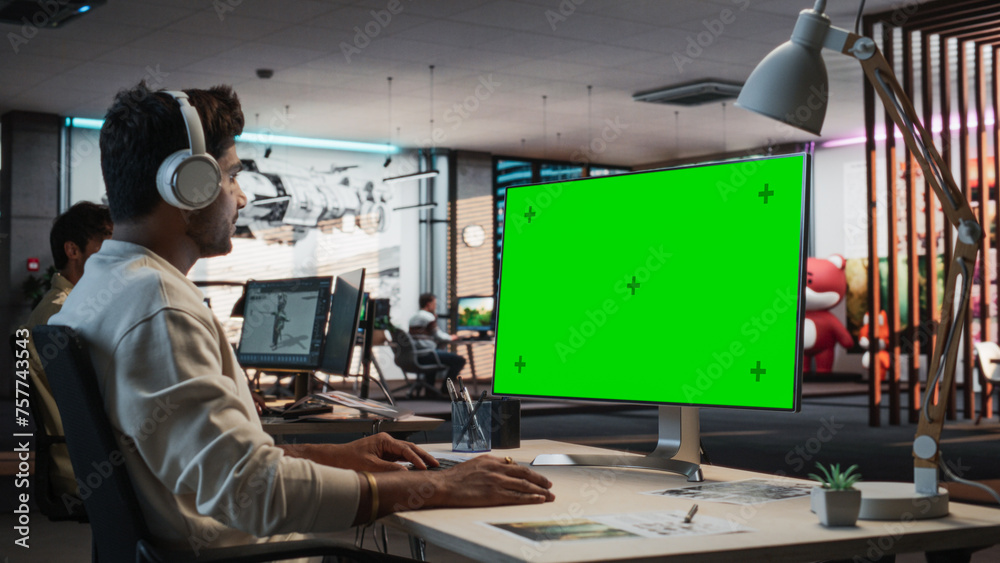 Aufkleber Indian Male Game Designer Using Desktop Computer With Green Screen Chromakey on Display, Designing Immersive World In 3D Modelling Software For New Video Game. Man Working In Game Development Office