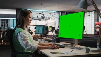 Female Asian Game Programmer Coding On Desktop Computer With Green Screen Chromakey On Display In...