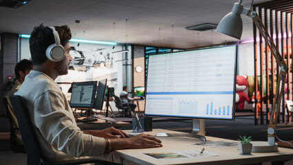 Indian Male Manager Using Desktop Computer With Analytics Software wth Financial Reports. Man Working In Game Development Company Diverse Office