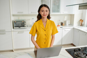 Portrait of cheerful smart teenage girl working on laptop at kitchen counter