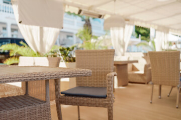 Wicker furniture tables in the open air are waiting for visitors. The interior of the restaurant in the open air. Empty tables of street cafe.
