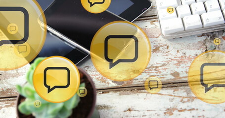 Image of yellow digital message icons flying up over electronic devices on wooden background