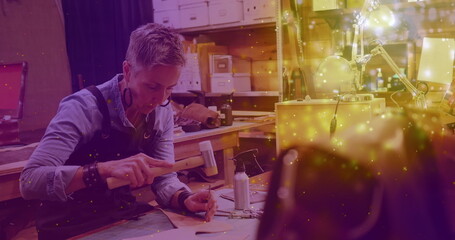 Image of glowing light over caucasian woman working in workshop