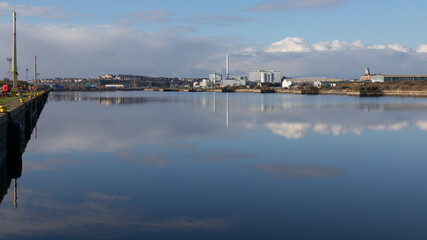 A view across the entrance channel at Barry Docks in South wales. Reflected in the water is  Barry Biomass Renewable Energy Plant and the town can be seen in the distance