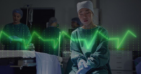 Image of cardiograph over asian female surgeon wearing medical gloves at hospital