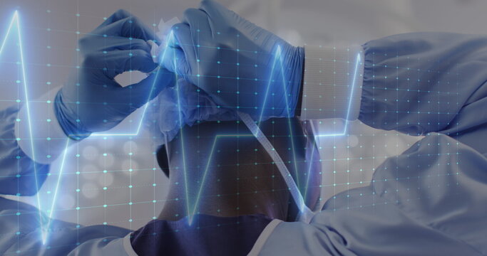 Image of cardiograph over african american male surgeon wearing face mask at hospital