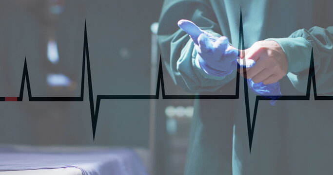Image of cardiograph over caucasian male surgeon wearing medical gloves at hospital