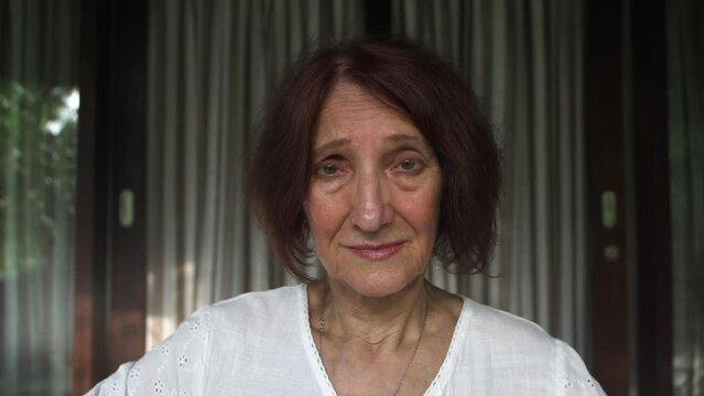 Close-up elderly woman with a sad pitiful unhappy expression looks at the camera, frustrated mature grandmother