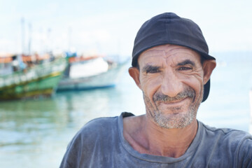 Fisherman, portrait and rugged man with smile, boats and fishing trawler in ocean. Wrinkles, aged...