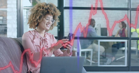 Blue and red graphs and arrows over happy biracial businesswomen using smartphone in office