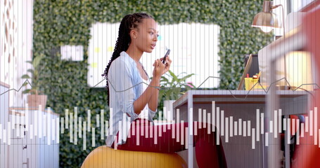 Image of data processing and diagram over biracial businesswoman talking on smartphone in office