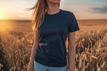 Caucasian female model wearing a navy blue crewneck blank mockup t-shirt with short sleeves in a field background at sunset , woman face is not visible - obrazy, fototapety, plakaty